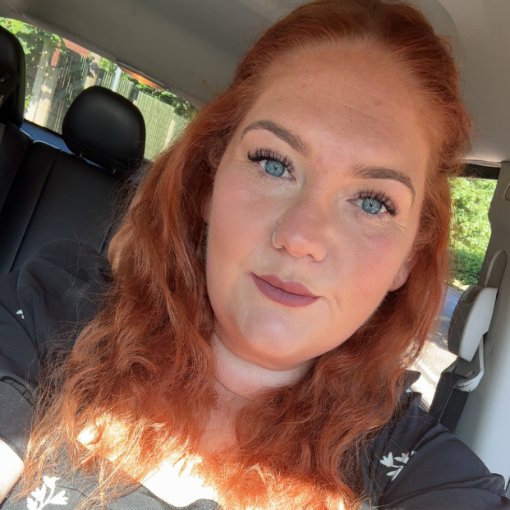 A woman with long red hair and blue eyes sits in a car, looking at the camera. Sunlight shines on her face and shoulder. A woman with long red hair and blue eyes sits in a car, looking at the camera. Sunlight shines on her face and shoulder.